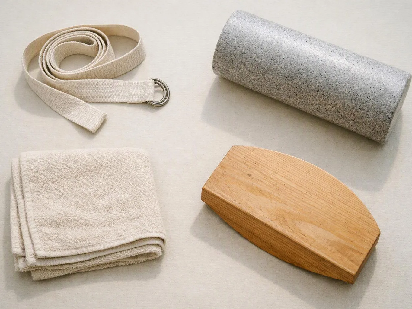 A coiled strap, rolled gray mat, folded towel, and wooden block rest on a light surface
