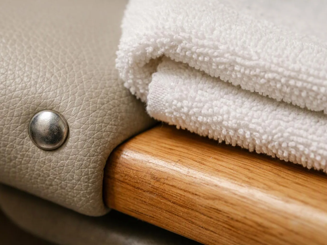 A rolled white towel rests beside a wooden handle and beige textured upholstery with a metal rivet